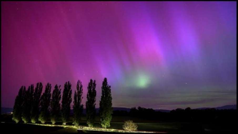 Northern lights glow in the night sky above the village of Daillens, Switzerland