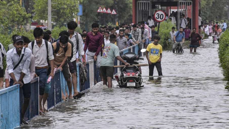 सूरत में भारी बारिश के बाद लोग पानी से भरी सड़क से गुजरते हुए।