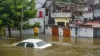 A man stands near a partially submerged vehicle due to...- India TV Hindi