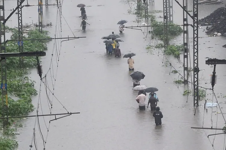 People walk on the waterlogged railway tracks during heavy...- India TV Hindi