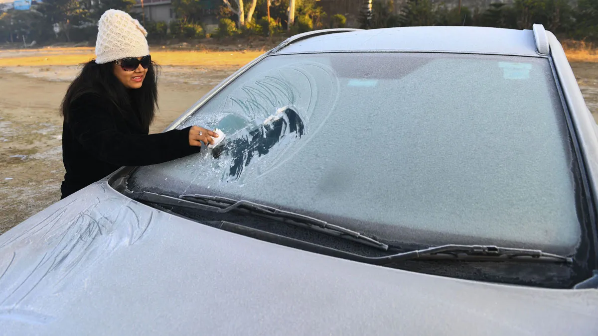 A tourist clears snow from her car's windshield during a...- India TV Hindi