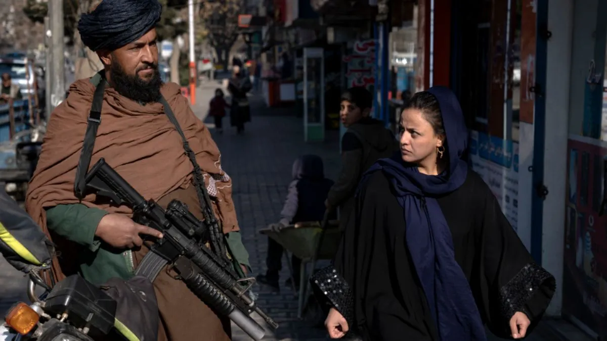 A Taliban fighter stands guard as a woman walks past in Kabul, Afghanistan- India TV Hindi