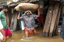 <p>A person carries a grain sack as his house gets flooded...- India TV Hindi