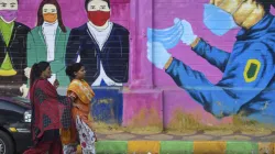 <p>Women walk past a graffiti on a wall urging people to...- India TV Hindi