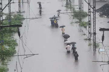 <p>People walk on the waterlogged railway tracks during...- India TV Hindi