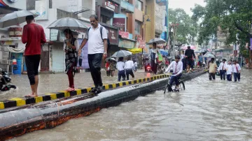 Pedestrians walk through a waterlogged road following heavy rainfall in Varanasi- India TV Hindi
