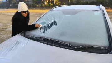 <p>A tourist clears snow from her car's windshield during a...- India TV Hindi