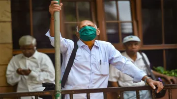 A man wears a mask as a preventive measure against coronavirus and watches stock prices on a screen - India TV Hindi