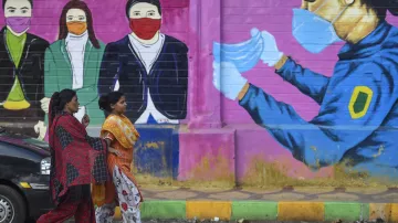 <p>Women walk past a graffiti on a wall urging people to...- India TV Hindi
