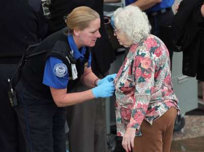 इस फोटो में सिक्युरिटी गार्ड एक बूढ़ी महिला के शर्ट के अंदर चैकिंग कर रही है।