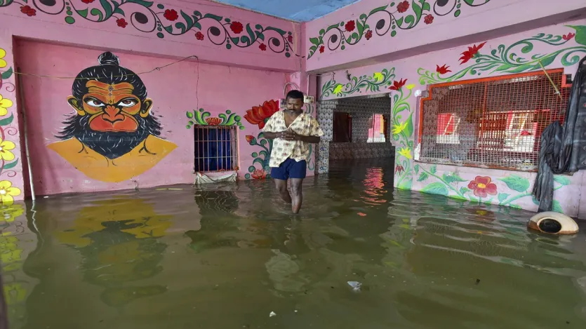 प्रयागराज में मंदिर परिसर में उफनती गंगा नदी के पानी से होकर गुजरता हुआ शख्स।
